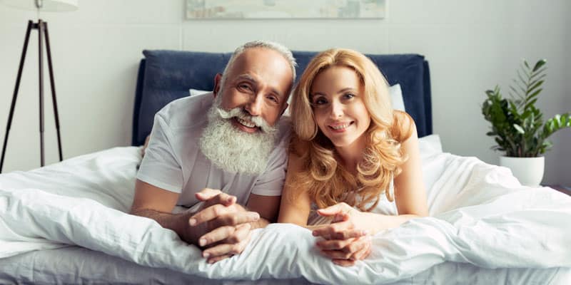 older guy and a young woman photographed on a bed