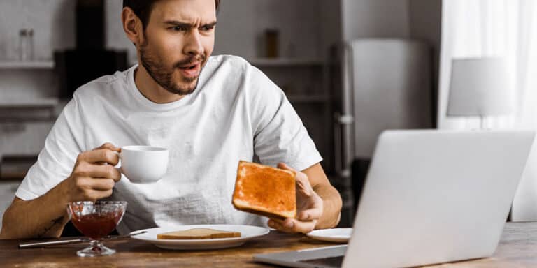 man eating breakfast in front of laptop